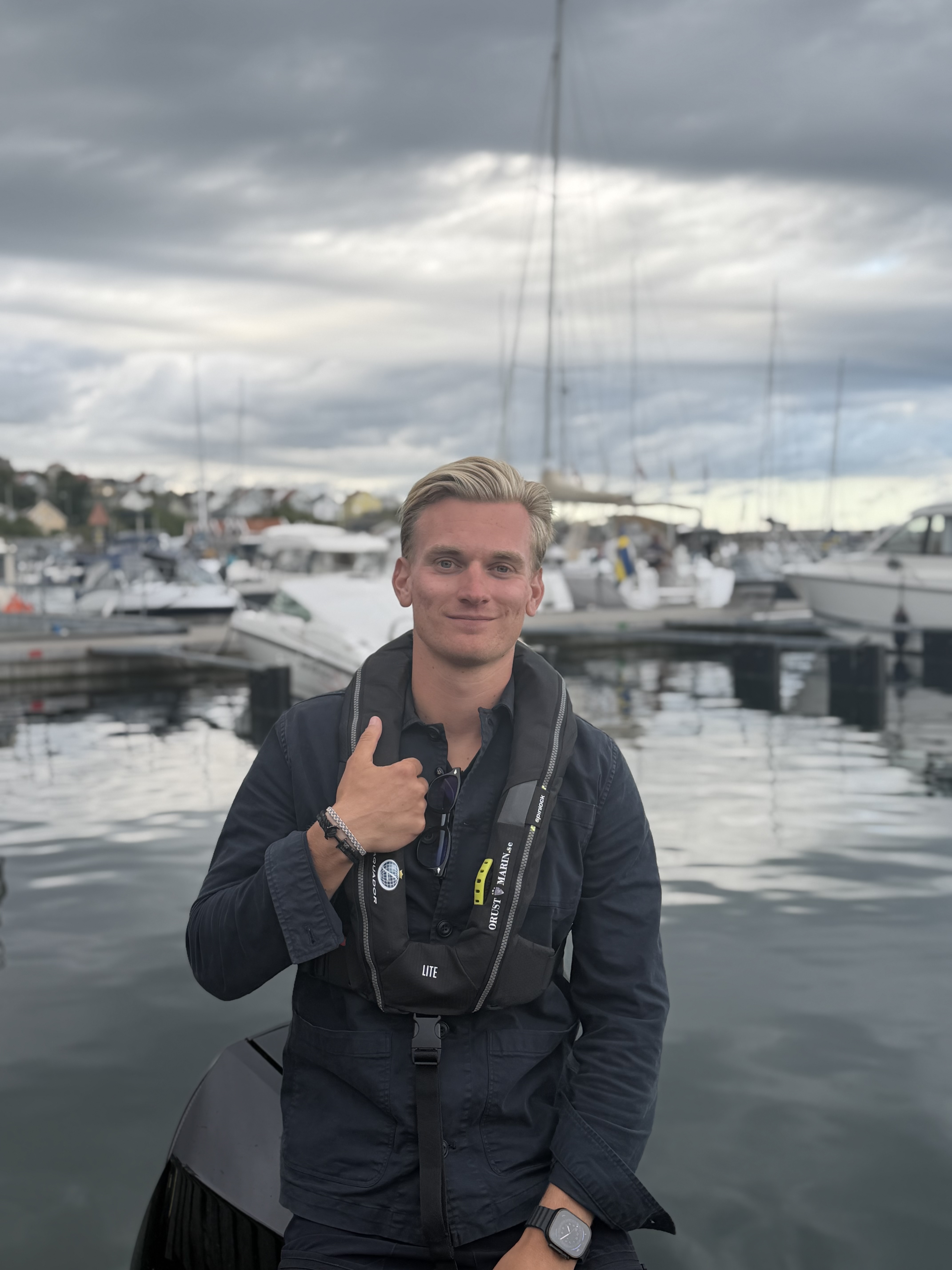 Erik Klavefors i hamnen på västkusten, med räddningsväst och segelbåtar i bakgrunden